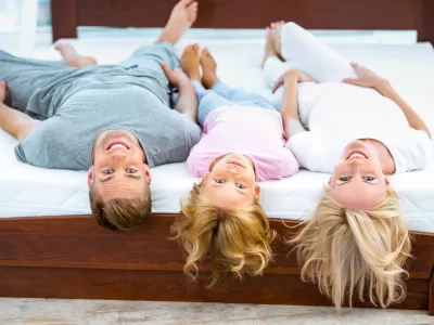 Photo of young family of three lying on nice white bed. Young family demonstrating quality of mattress
