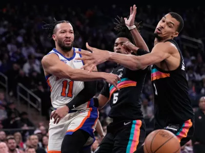 New York Knicks' Jalen Brunson, left, passes around San Antonio Spurs' Victor Wembanyama, right, and Stephon Castle during the first half of an NBA basketball game Sunday, March 1, 2026, in New York. (AP Photo/Seth Wenig)