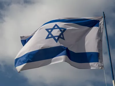 The flag of Israel against a blue sky with white clouds on a sunny day.