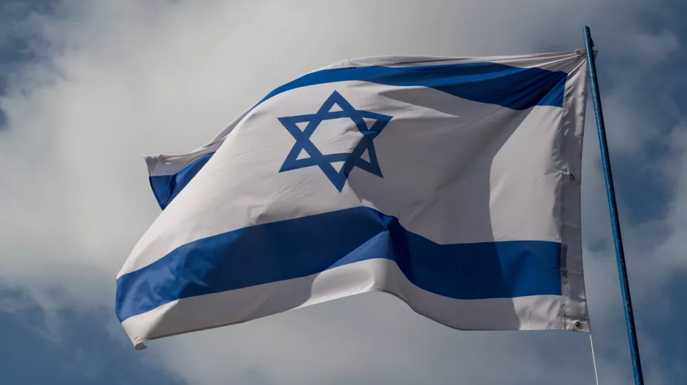 The flag of Israel against a blue sky with white clouds on a sunny day.