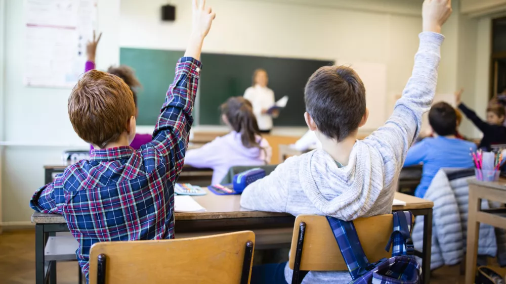 Schoolchildren at classroom with raised hands answering teacher's question.
