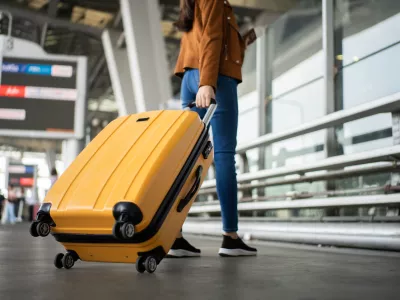 Close up of unrecognized woman tourist walking with her luggage through international airport terminal during holiday trip, female tourist rolling suitcase alone.