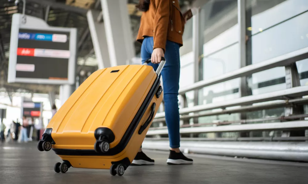Close up of unrecognized woman tourist walking with her luggage through international airport terminal during holiday trip, female tourist rolling suitcase alone.